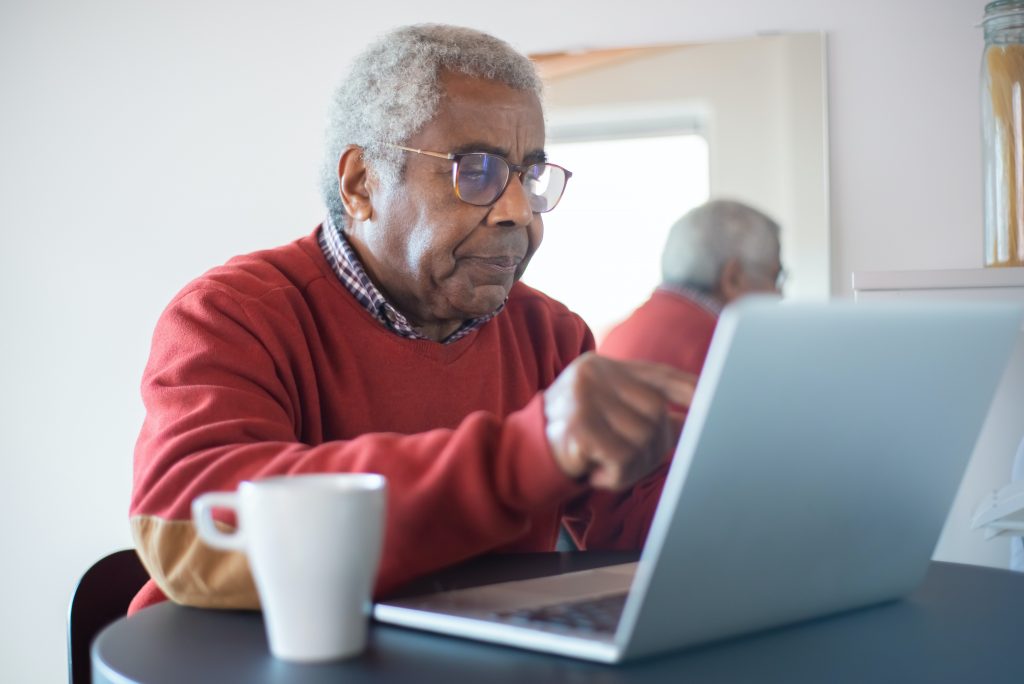 Hombre de edad avanzada, con suéter rojo, utilizando su computador portátil. 